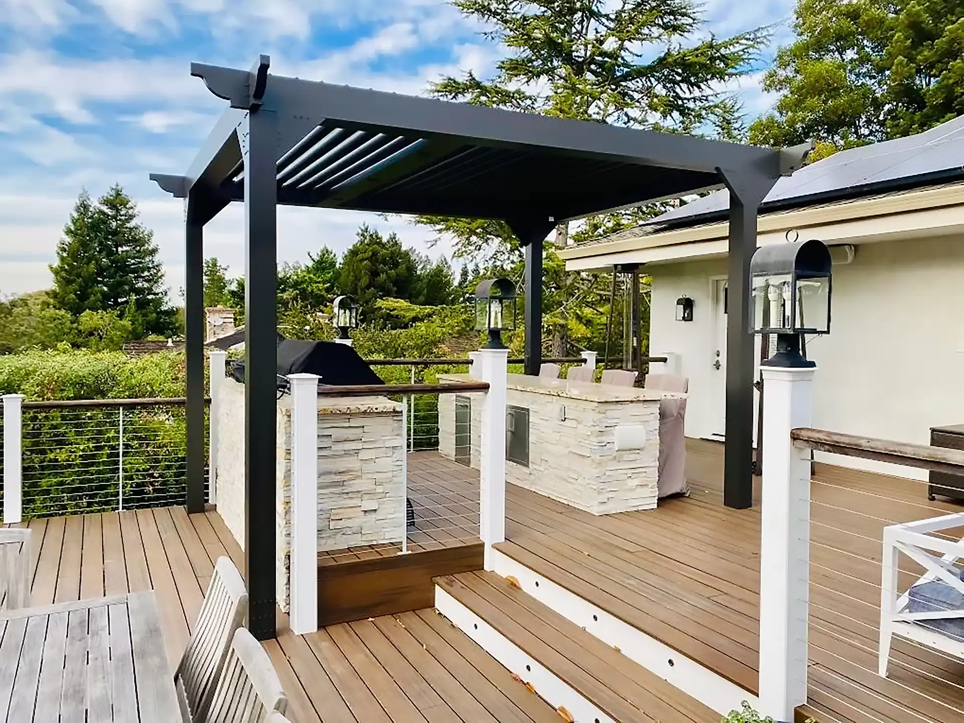 photo of multi-level deck with a pergola and outdoor kitchen